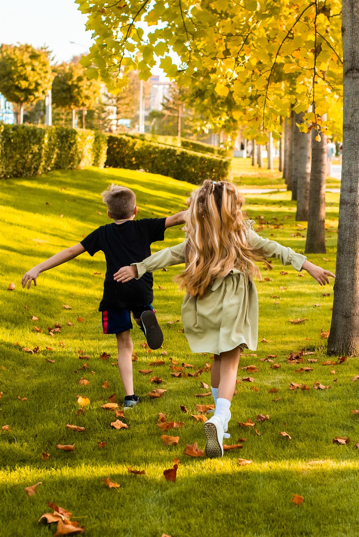 Bambini che corrono in un parco con le braccia aperte, tra erba e foglie